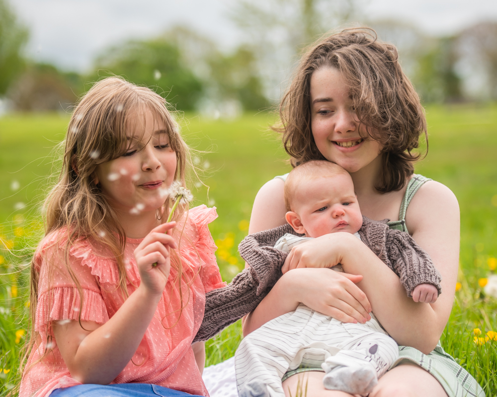 Sisters blowing dandelions in grass, Graves Park Sheffield family portraits