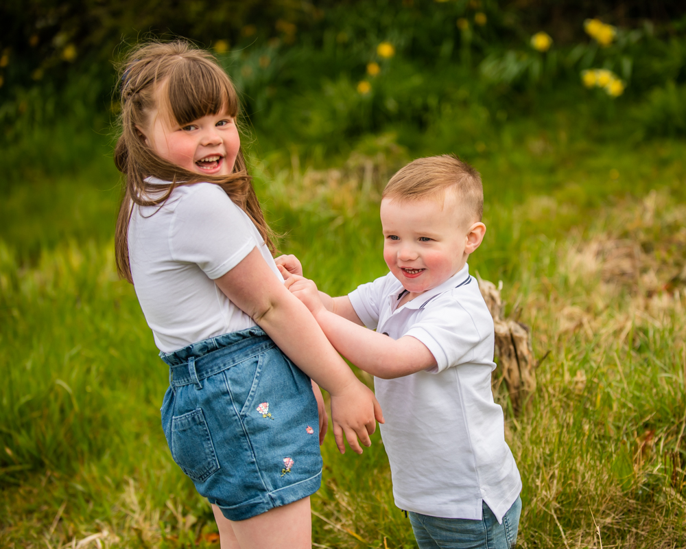 Toby and Lucy holding hands in spring flowers. Fletchertown portraits, Cumbria
