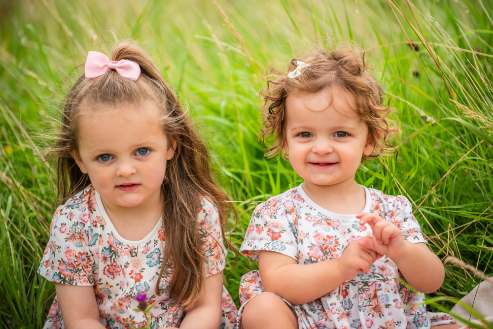 Sisters smiling in long grass, Wigton family photographers Cumbria